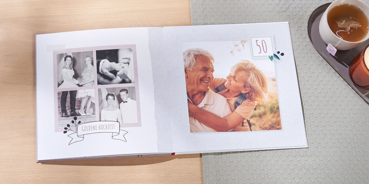 Auf einem Tisch liegt ein offenes CEWE FOTOBUCH. Links sieht man alte Schwarzweissbilder eines frisch vermählten Ehepaars auf ihrer Hochzeit vor 50 Jahren. Rechts ist ein aktuelles Bild vom Ehepaar am 50. Jahrestag zu sehen. Neben