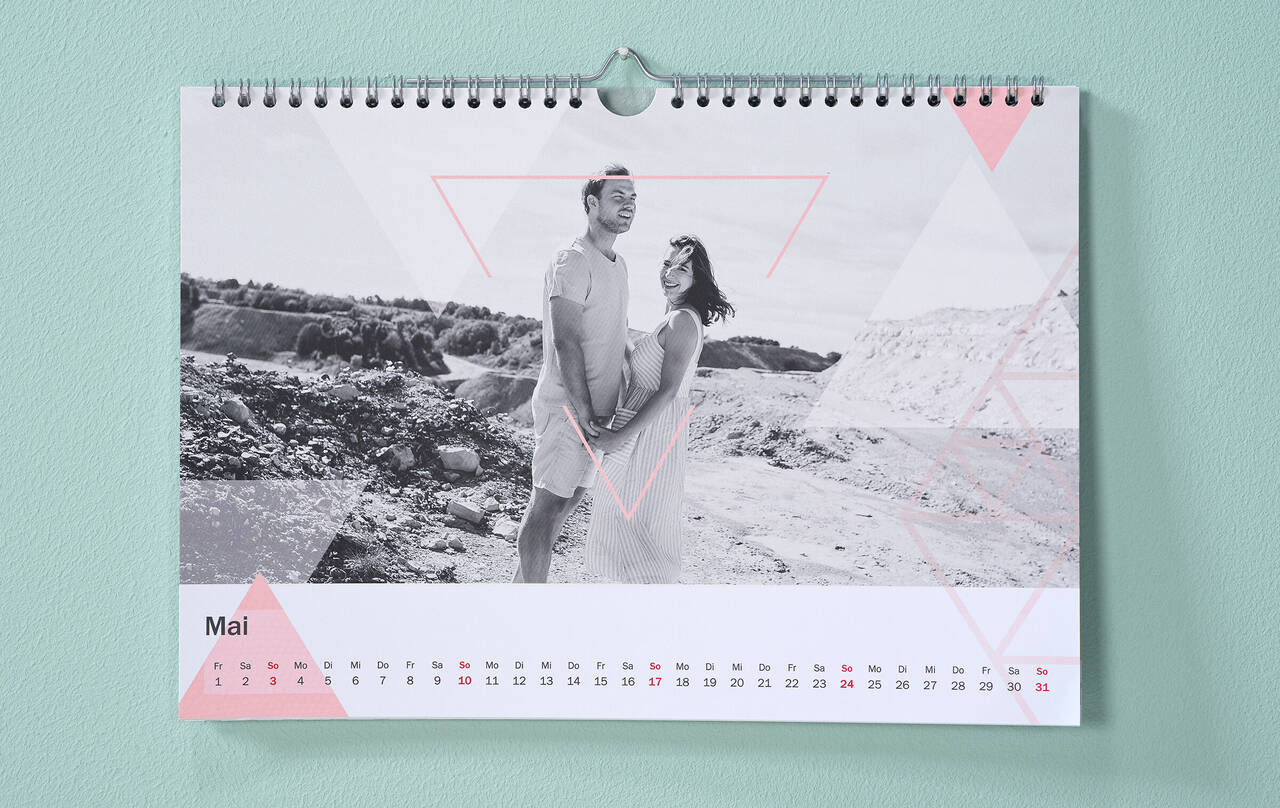 Kalender mit Pärchenfoto in Schwarz-Weiss und dreieckigen Cliparts in Pastell hängt an mintgrüner Wand.