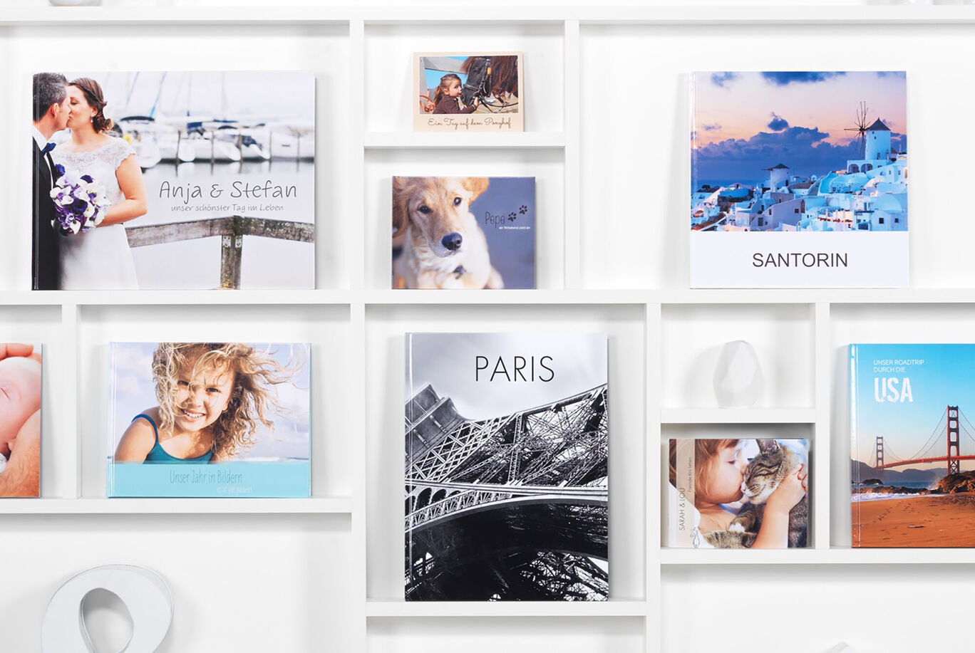 Various photo books on a shelf, including the CEWE PHOTO BOOK titled 'Paris' and another titled 'Santorini'.