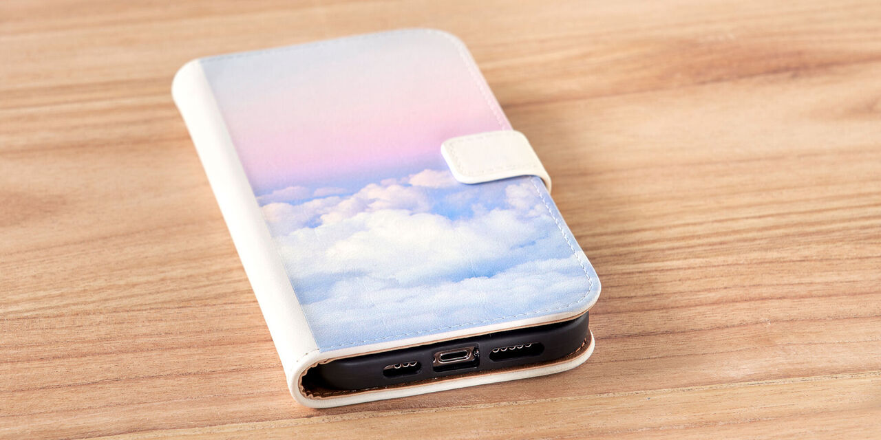 Un smartphone est posé sur une table. On y aperçoit la coque du smartphone, sur laquelle on peut voir une photo de nuages de couleur rose. Il s’agit d’un étui sideflip en cuir blanc.