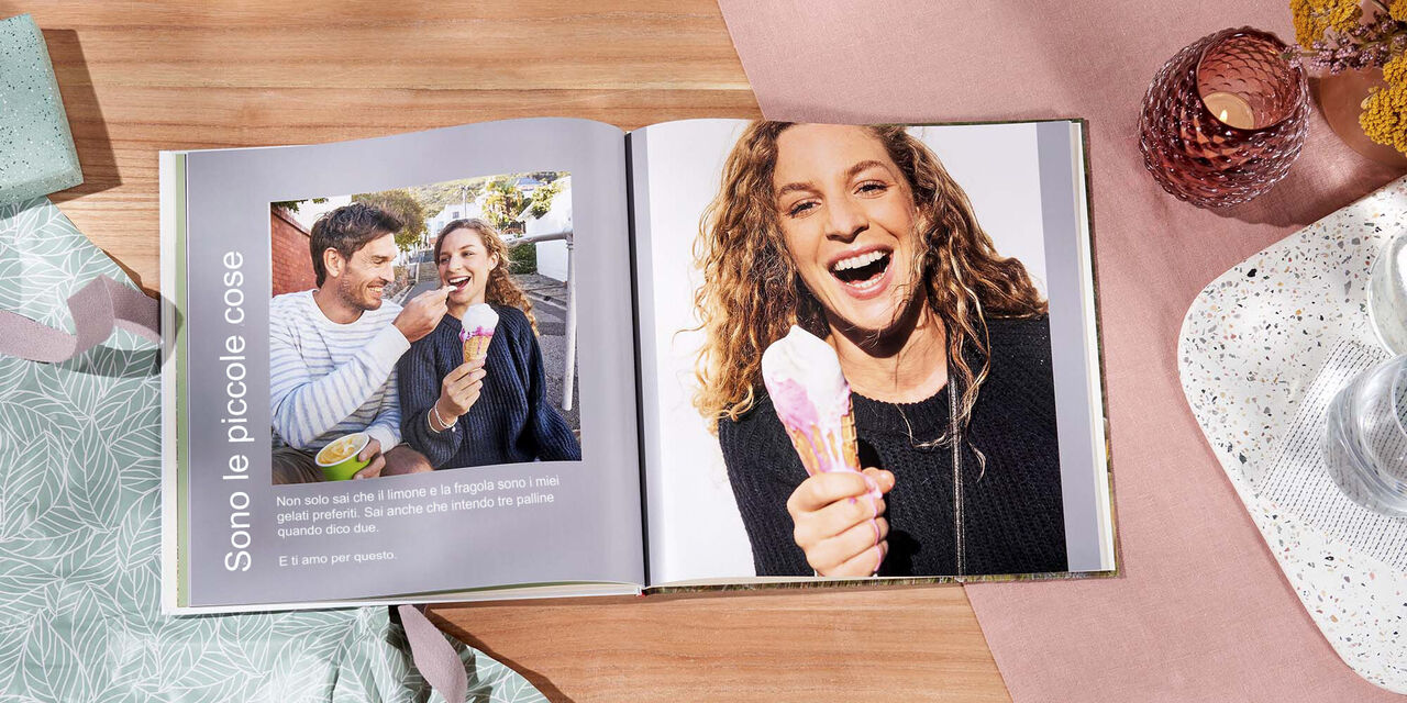 Su un tavolo c’è un FOTOLIBRO CEWE aperto. Una pagina mostra la foto di una coppia, l’altra quella della donna che mangia un gelato. A sinistra c’è la didascalia «Sono le piccole cose».